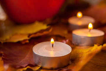 Composition with pumpkins and candles on maple leaves on wooden background. Side view. Selective soft focus.
