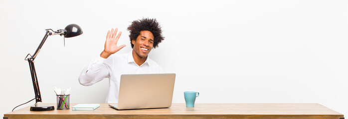 young black businessman smiling happily and cheerfully, waving hand, welcoming and greeting you, or saying goodbye on a desk © kues1