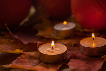 Composition with pumpkins and candles on maple leaves on wooden background. Side view. Selective soft focus.