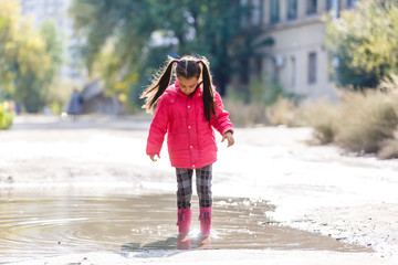Adorable little girl standing in a puddle on warm autumn day