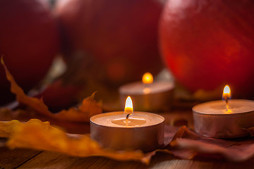 Composition with pumpkins and candles on maple leaves on wooden background. Side view. Selective soft focus.