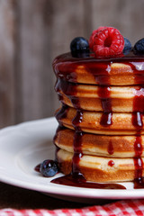 Delicious pancakes with fresh berries and syrup on wooden table, closeup