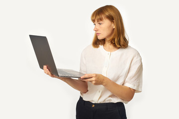 Fototapeta premium Headshot of young woman with red hair and freckles holding laptop and looking at the screen working. Isolated on white background with copyspace
