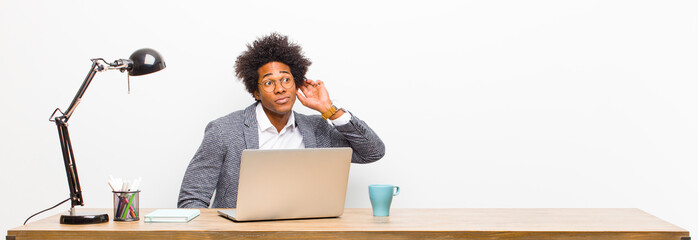 young black businessman looking serious and curious, listening, trying to hear a secret...