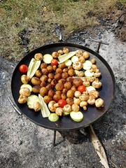 Baked potatoes, mushrooms, bell peppers, zucchini and tomatoes in a pan, on a fire
