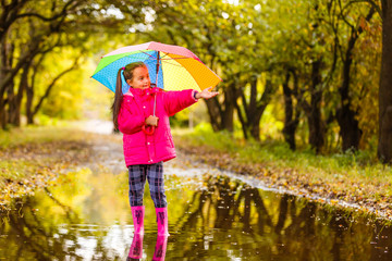Playful little girl hiding behind colorful umbrella outdoors