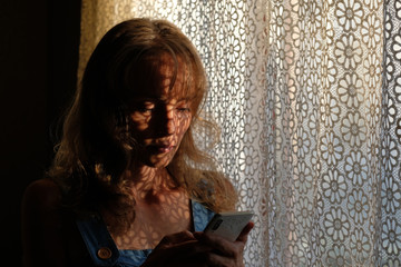 Beautiful young girl looks at the phone. The play of light and shadow on the body. Light shadow picture.