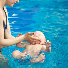 Swimming lessons for newborns with mothers in paddling pool. Blue turquoise water on background. Parental care and parenting, healthy lifestyle, wellness program, water rehabilitation, aquatherapy