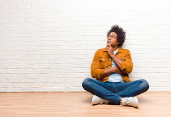 young black man with a concentrated look, wondering with a doubtful expression, looking up and to...