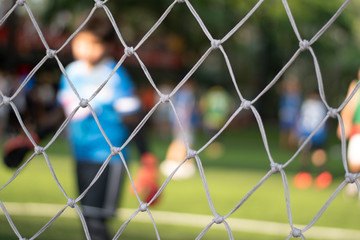 Fototapeta premium Soccor goal net with Asia school kids team playing football with young boys player in ball match field in sport club as background.