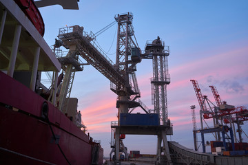 Fototapeta na wymiar Grain terminal at sunset. Dock crane and bulk carrier ship at sunset