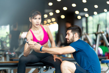 Trainer or instructor man is teaching asian spoty woman lifting a dumbbell and exercise in the gym. Smiling Woman Using Hand Weights While Personal Trainer Supervises Her Progress