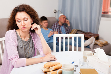 Upset woman on background with relaxed husband and son