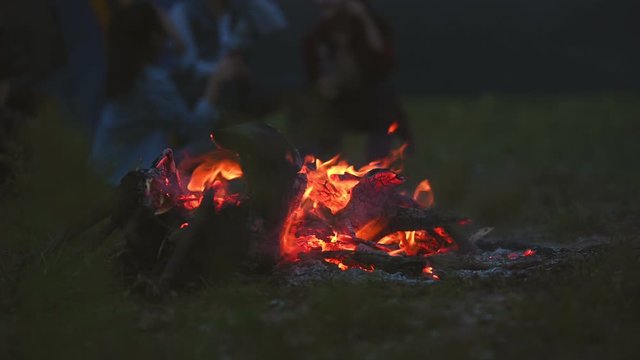 Campfire in the night with camping people background in meadow field on picnic. Bonfire in dark. Orange and yellow fire energy fuel. 4K motion video footage