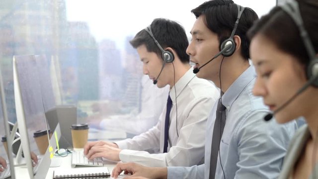 Young Asian male telemaketing operator with team working at call center office in the city