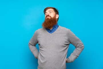 Redhead man with long beard over isolated blue background suffering from backache for having made...