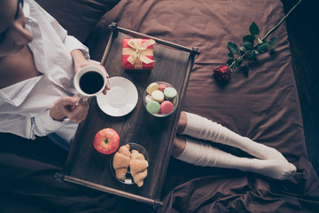 Cropped top above high angle view of nice attractive lovely girl sitting on bed long legs wearing gaiters drinking coffee eating fresh delicious snack on sheets linen house flat apartment