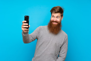 Redhead man with long beard over isolated blue background making a selfie