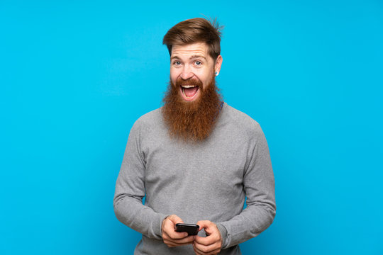 Redhead Man With Long Beard Over Isolated Blue Background Surprised And Sending A Message