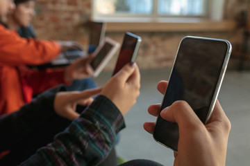 Group of happy young young people sitting on a sofa together. Sharing a news, photos or videos from smartphones, reading articles or playing games and having fun. Social media, modern technologies.