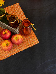 Top view of glass bottles with autumn leaves and apples over dark concrete background and copy space in portrait position 