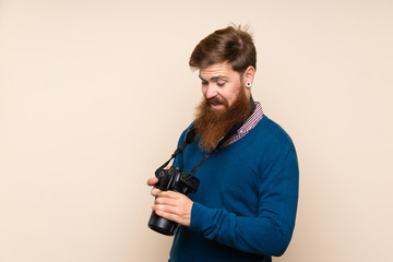 Redhead man with long beard over isolated background with a professional camera