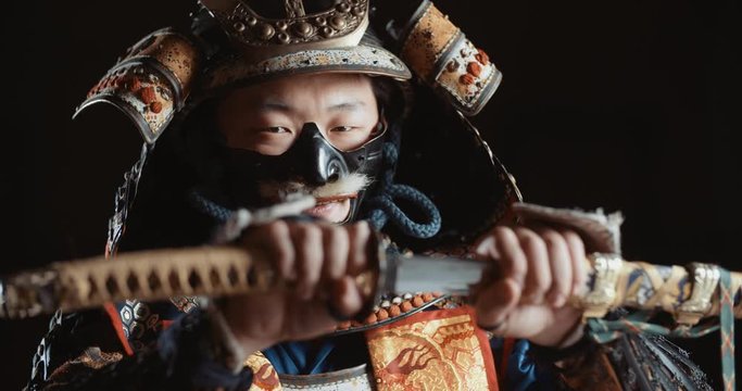 Man in traditional japanese samurai clothing is looking at camera and demontrating his katana sword, isolated on black background - culture, tradition, martial arts concept 4k footage