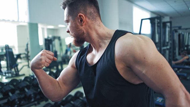 Athletic man model posing at gym. Bodybuilder demonstrating his arm strength at gym