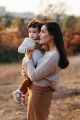 Cute curly baby boy hug his lovely mom in autumn park, closeup portrait woman with son looking up...