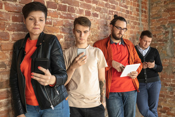 Group of happy caucasian young people standing behind the brick wall. Sharing a news, photos or...