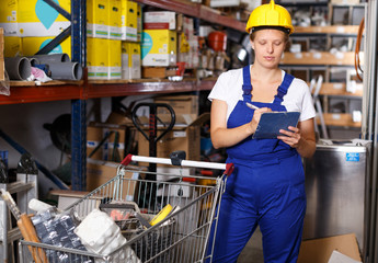 Young woman in uniform looking construction  materials with notebook and  basket
