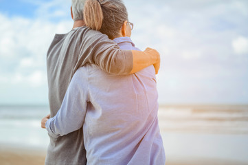 A senior couples embrace the beach in the morning, look at the bright blue skies and plan life insurance with a happy retirement concept.