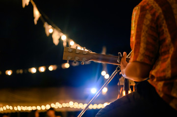 Rear view of the man sitting play acoustic guitar on the outdoor concert with a microphone stand in...