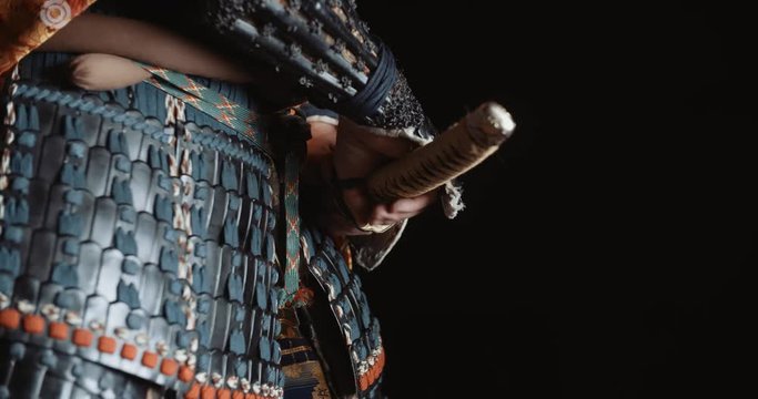 A man in japanese samurai armour is taking a sword out of his scabbaders, isolated on black background - martial arts, culture, traditions concept 4k footage