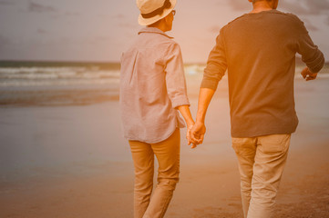 A retired couple walk hand in hand at the beach at sunrise,plan life insurance at retirement...