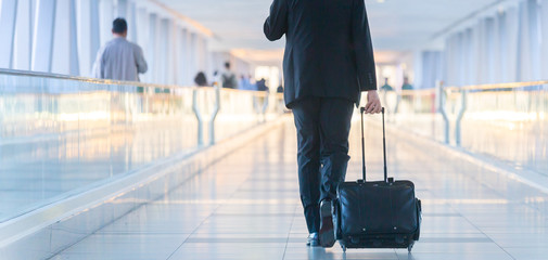 Rear view of unrecognizable formaly dressed businessman walking and wheeling a trolley suitcase at...