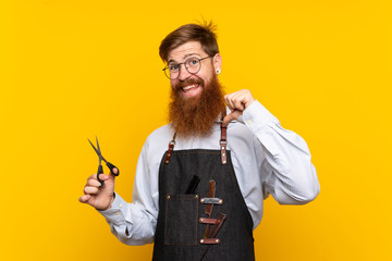 Barber with long beard in an apron over isolated yellow background proud and self-satisfied