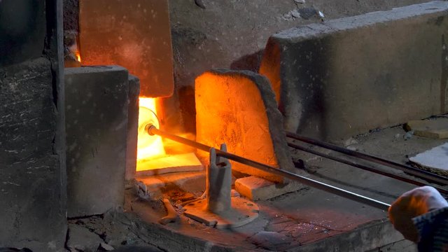 Glassblower heats a glass vase in a red hot industrial furnace