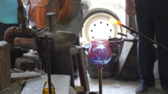 Skilled artist heas molten glass in a furnace then shapes a handle on top of the glowing pot