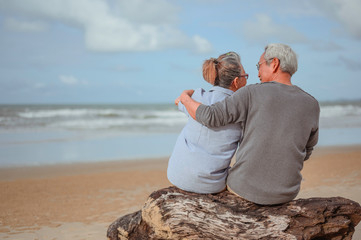 A retired couple sitting at the sea, a woman pointing a finger for a man to watch something on the...