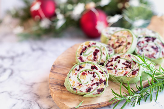 Fresh homemade cranberry pinwheels made with cream cheese, dried cranberries, walnuts, goats cheese and rosemary ready for the holidays. Selective focus with blurred background.