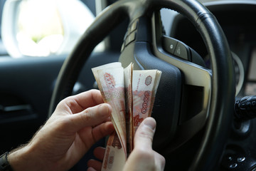 Banknotes five thousand Russian rubles in the hand on the steering wheel of a car. Cash paper...