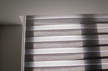 Details of brown fabric roller blinds on the plastic window with wood texture in the living room.