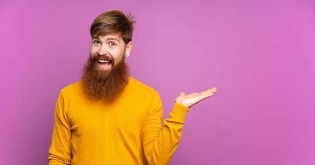 Redhead man with long beard over isolated purple background holding copyspace imaginary on the palm...