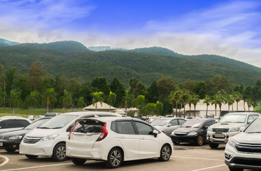 Car parking in large asphalt parking lot with trees, white cloud and blue sky mountain background