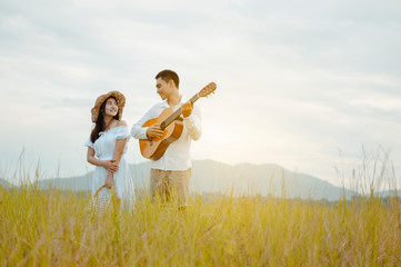 Happy lovers stand on the grassland looking at each other with tenderness. Men play guitars to...