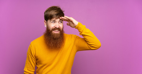 Redhead man with long beard over isolated purple background looking far away with hand to look...