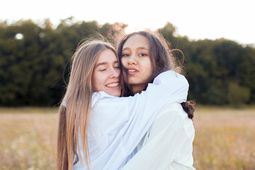 Fototapeta premium Two young women in white shirts hugging outdoors. Best friends
