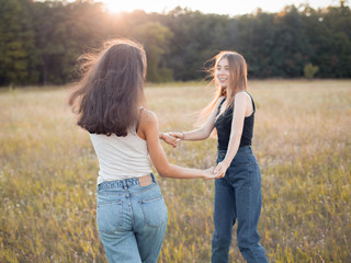 Two happy young women dancing on the autumn field under sunlight
