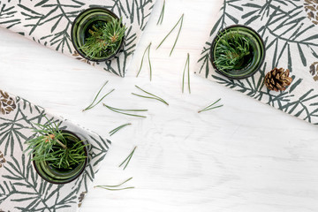 Three green glass vases with pine branches on white painted wooden background.